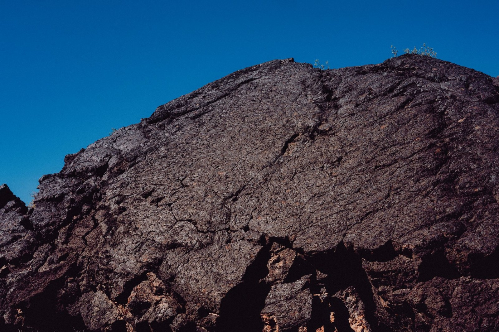 Close-up of an eroded, textured rocky surface beneath a clear blue sky, showing natural geology.